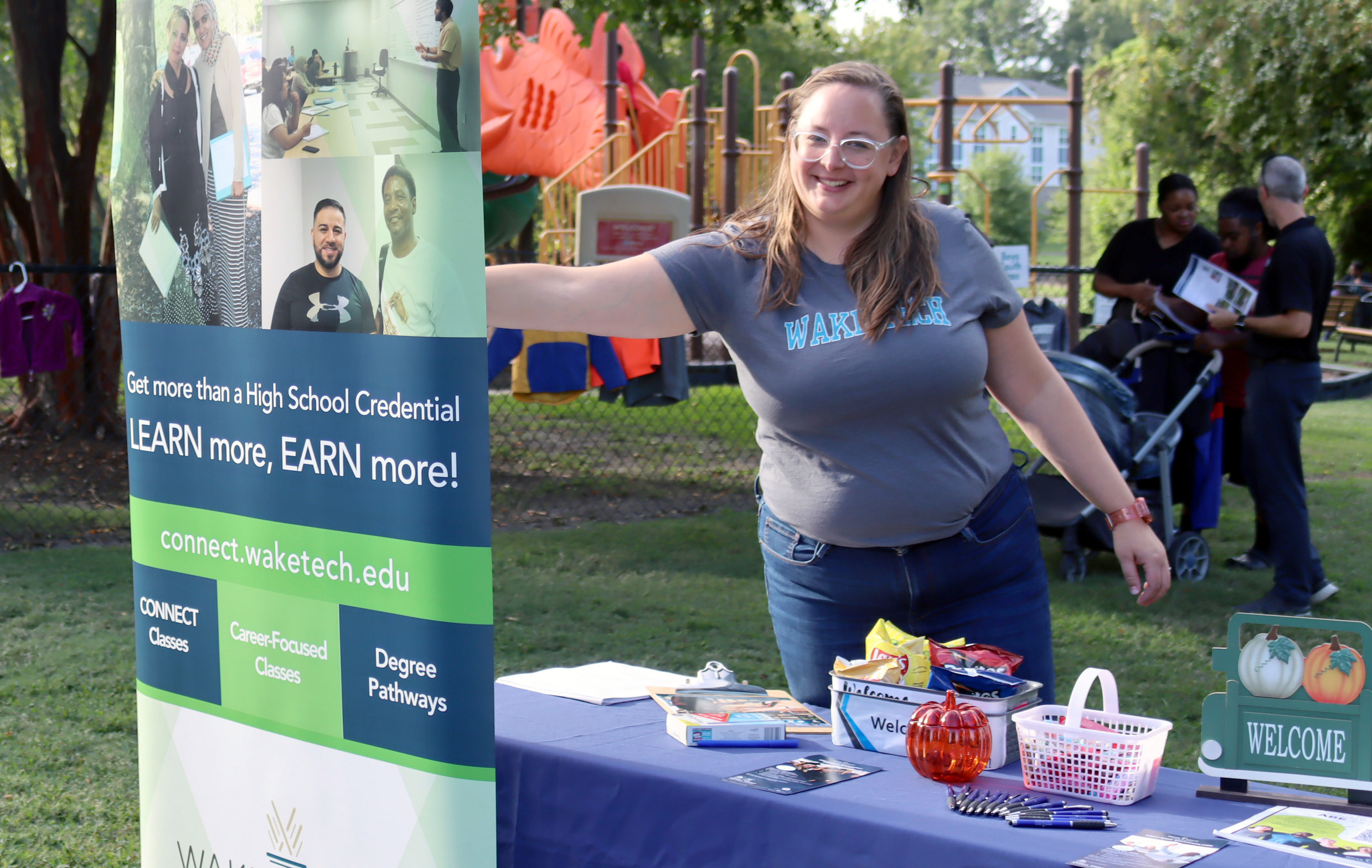 Smiling woman at a table beside a pop-up banner promoting Wake Tech.